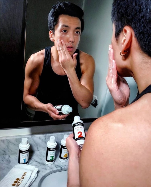 Metrin customer holding #2 Lathering Cleanser smooths product onto face while looking into mirror with perfect skin. Enjoys the after effects of the perfect shave.