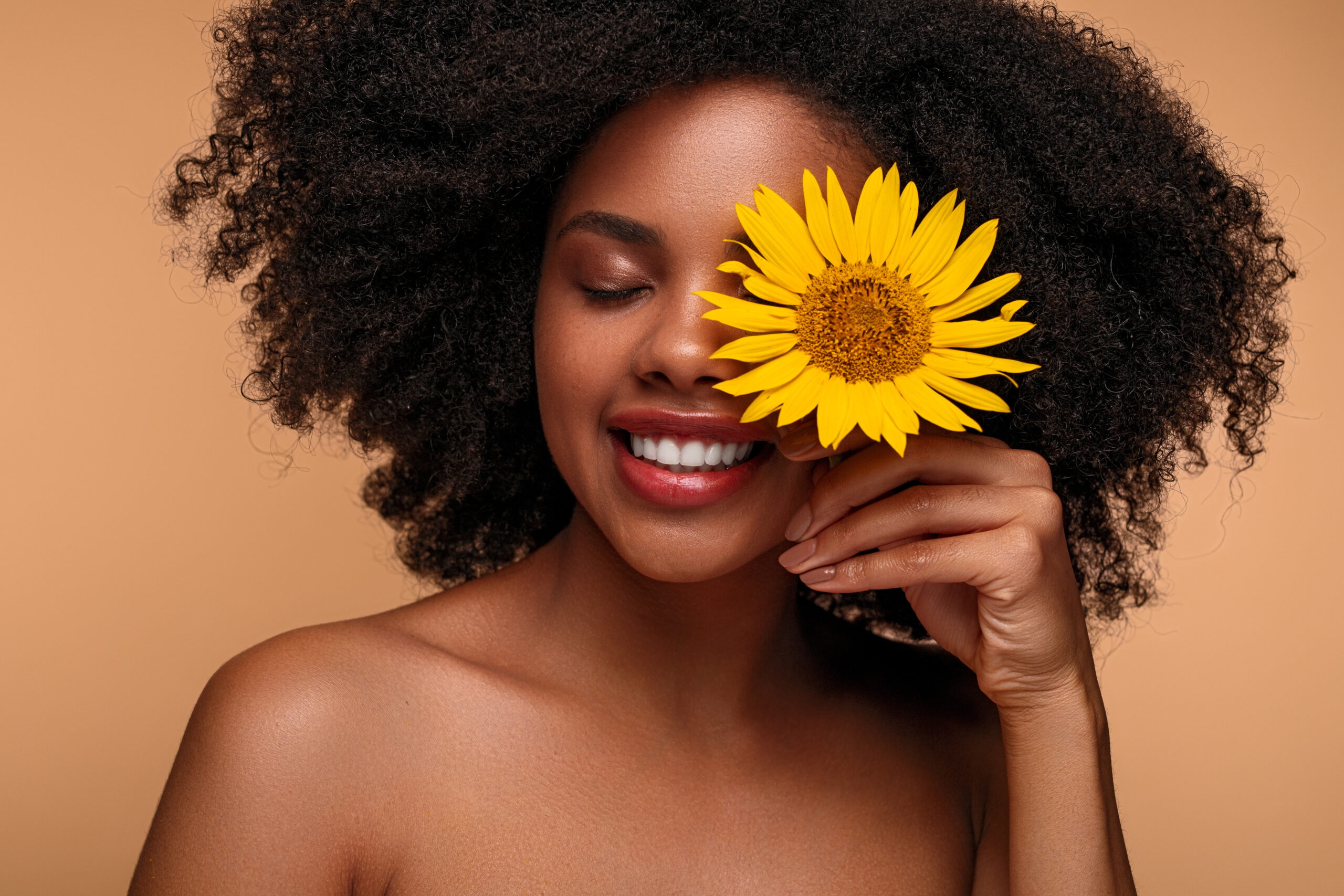Woman with Sunflower infront of face, enjoying the benefits of Vitamin E the best Vitamin for skin